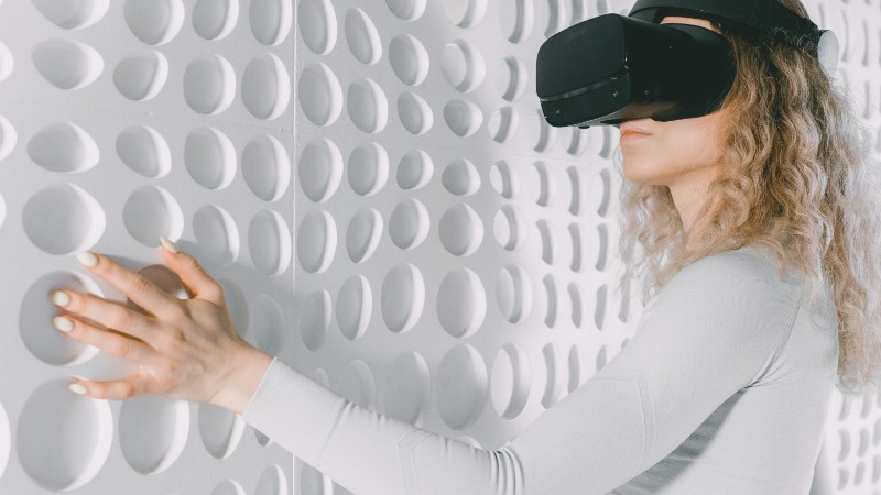 Woman explores a white textured wall using virtual reality headset, capturing advanced tech and tactile perception., tags: und - pexel